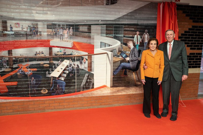 Renée and Lester Crown standing in front of image on brick wall of future Schine Student Center renovation