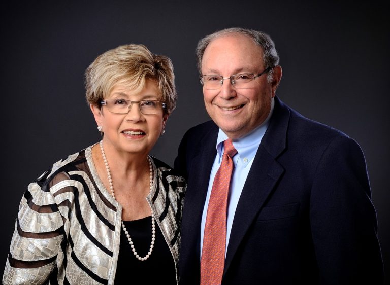 Diane and Robert Miron standing together in front of a solid dark background
