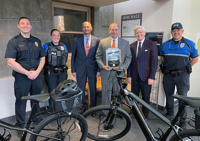 Jay Gelb, DPS Quartermaster, Officers and Chief and Chief Student Experience Officer stand in a building behind two electric bikes.