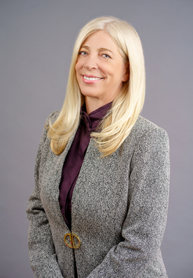 Laura Feldman in grey suit standing in front of a solid grey purple background