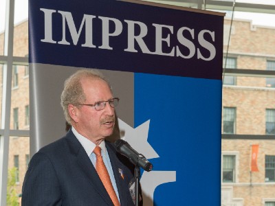 Kenny Goodman standing in front of an IMPRESS sign